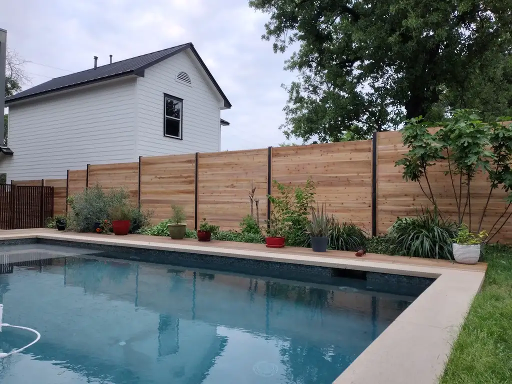 Horizontal cedar privacy fence behind a pool with planted beds along its base