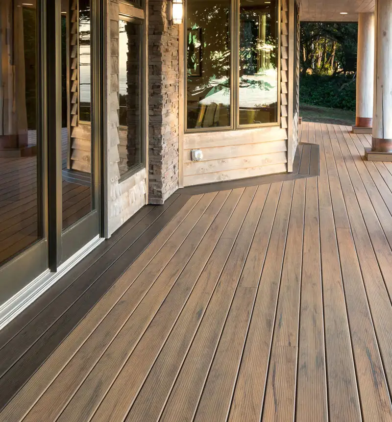 Deck boards running level from the sliding glass doors along the back of a stone and wood home