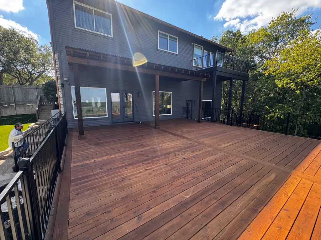 Large stained wood deck with black metal railing across the back of a two-story home