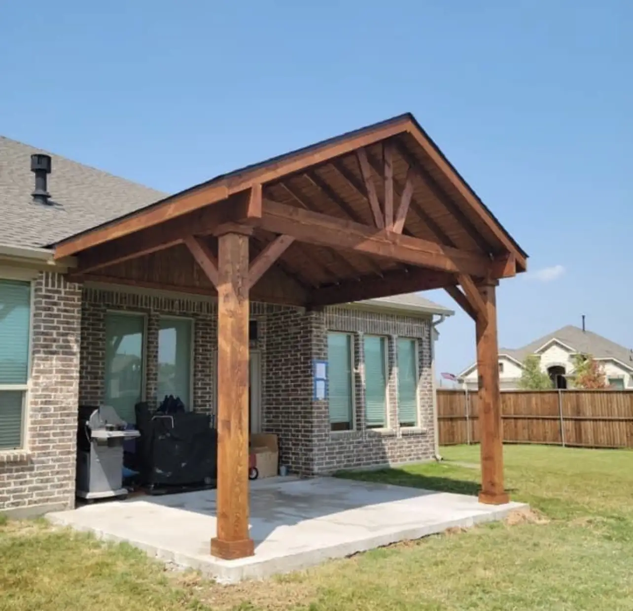 Attached cedar gable patio cover extending from the back of a brick home