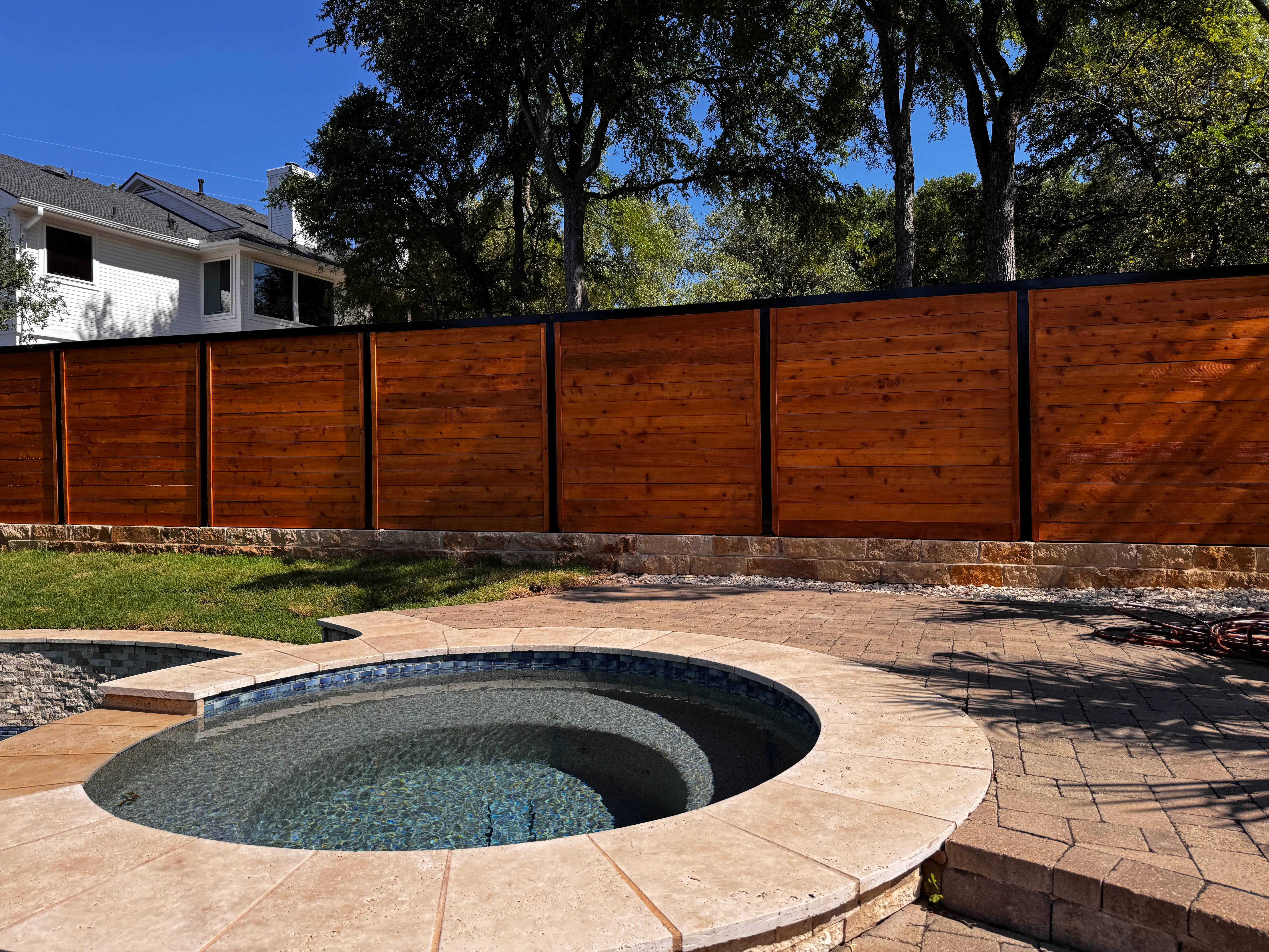Stained horizontal cedar fence with black steel posts on a stone wall behind a pool and spa