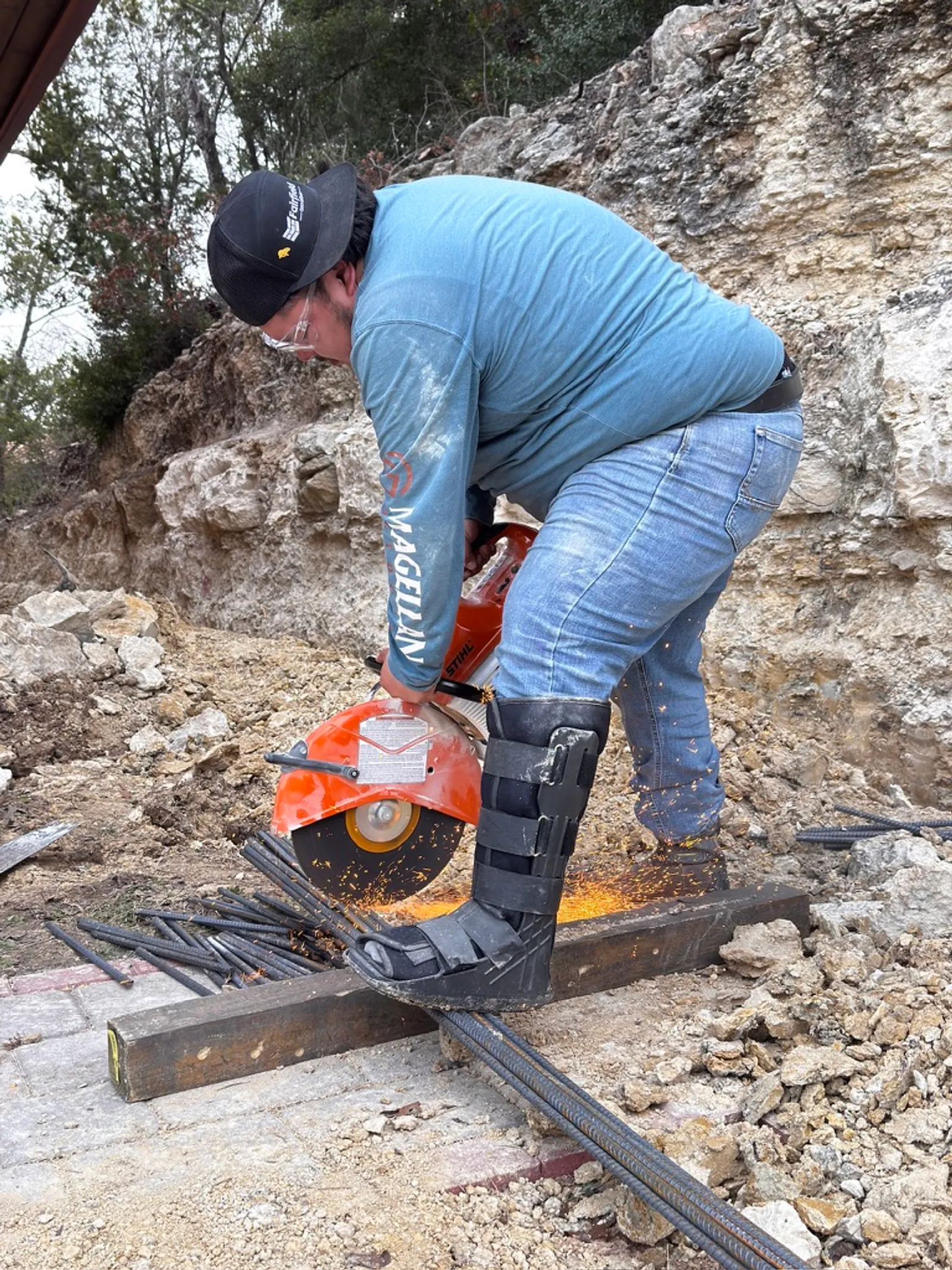Fairfield Innovations project manager in an ankle boot cutting rebar with a cut-off saw on an active job site in Austin, TX